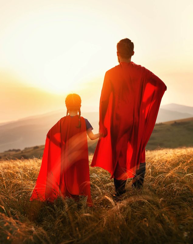 Far og datter med supermannkapper i soloppgang